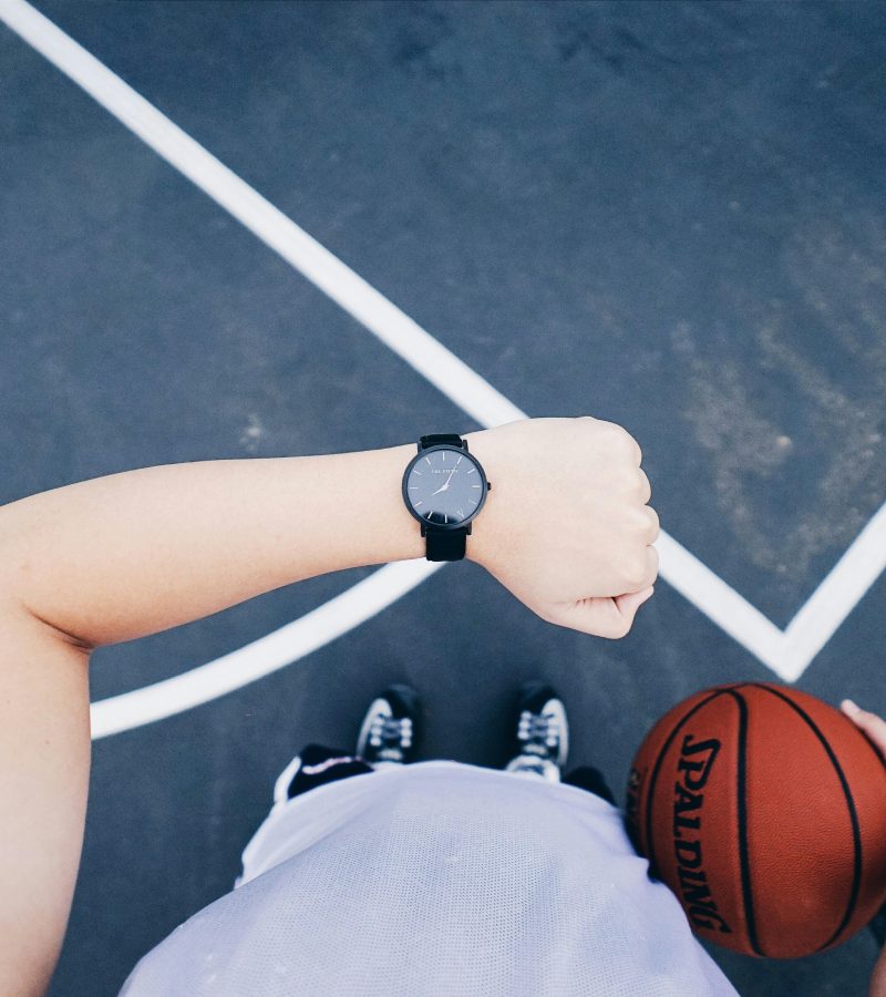 A basketball player checks their wristwatch while holding a ball on an outdoor court.