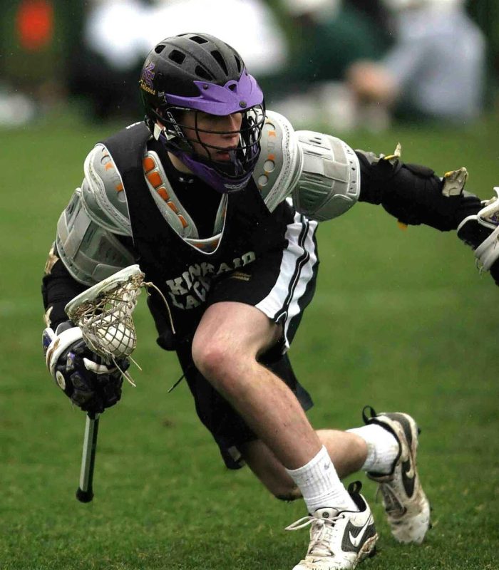 Dynamic shot of a lacrosse player mid-action during a sports game.