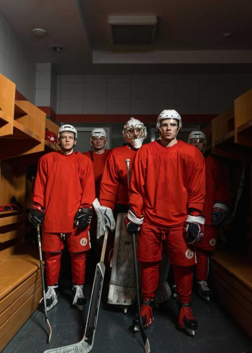 Team of hockey players in red uniforms standing in locker room with gear.